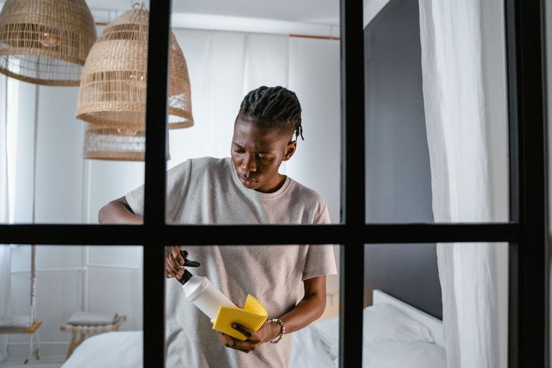 A man with a spray bottle and yellow cloth cleaning in a bright bedroom